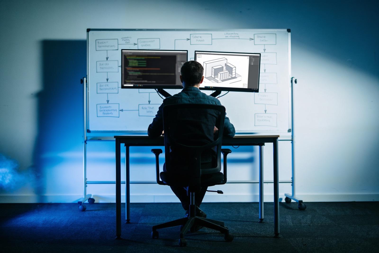 Illustrative: an engineer's desk with code and a system diagram on two monitors