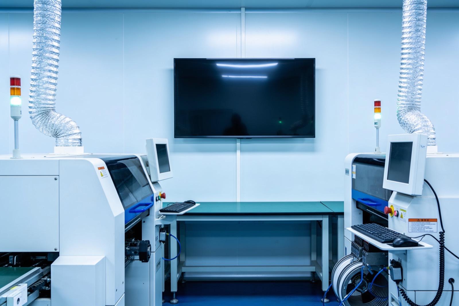 Illustrative: a plant floor dashboard on a wall-mounted TV beside production equipment