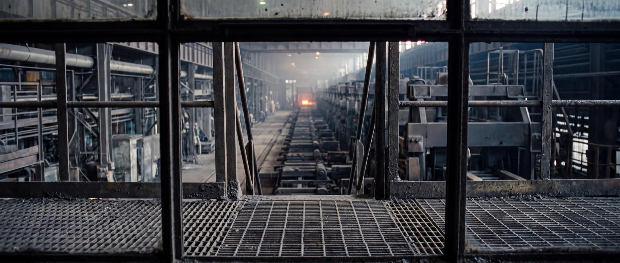 Illustrative: a hot strip mill at night from the pulpit, the line receding into heat shimmer — the environment a radar instrument has to survive